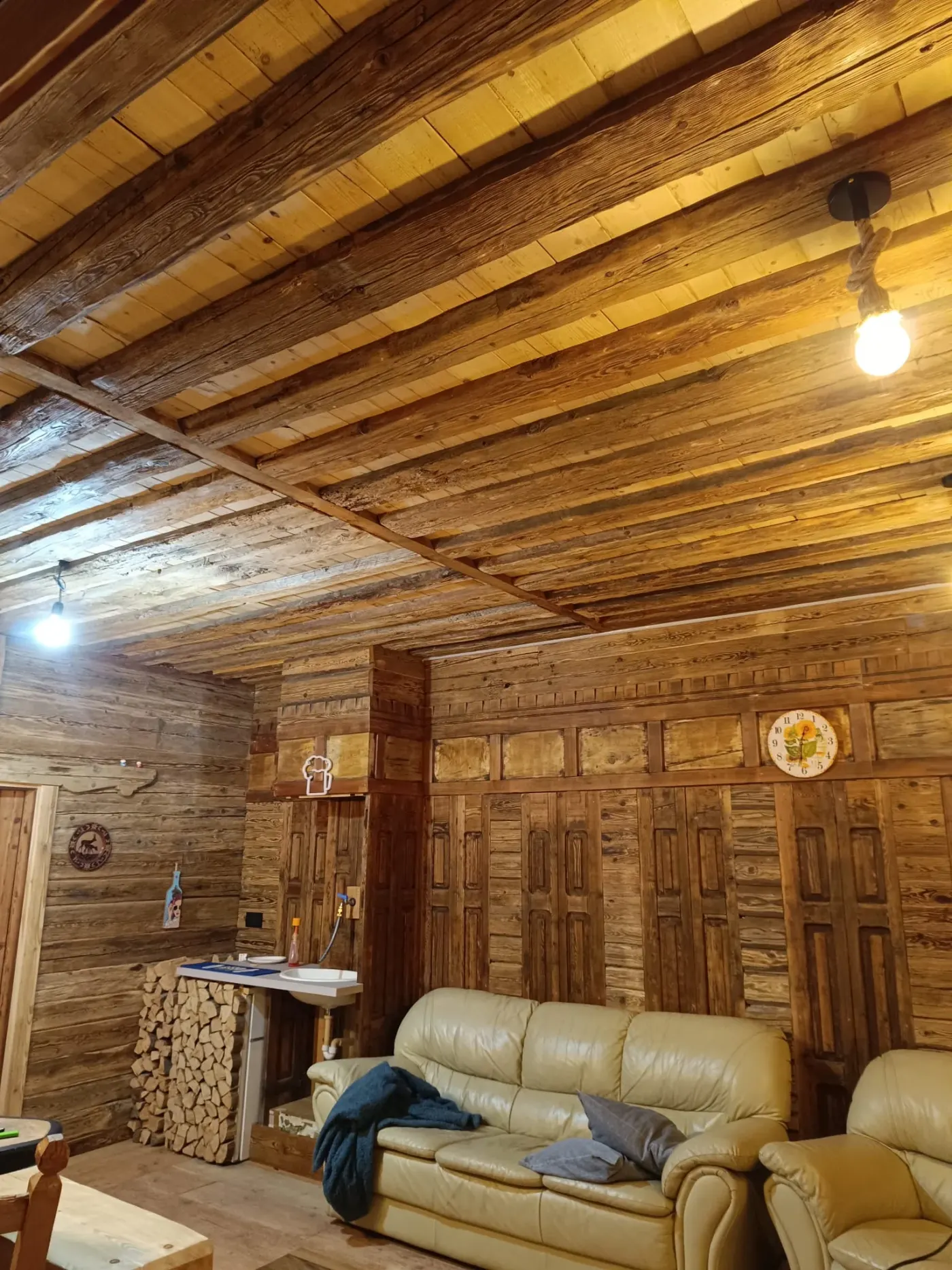 Soggiorno con travi a vista e boiserie in legno antico recuperato, divani in pelle e angolo cottura