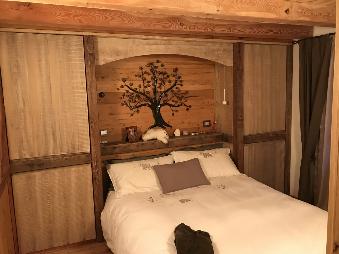 Letto matrimoniale incassato in una nicchia di legno antico con decorazione ad albero intagliata a mano