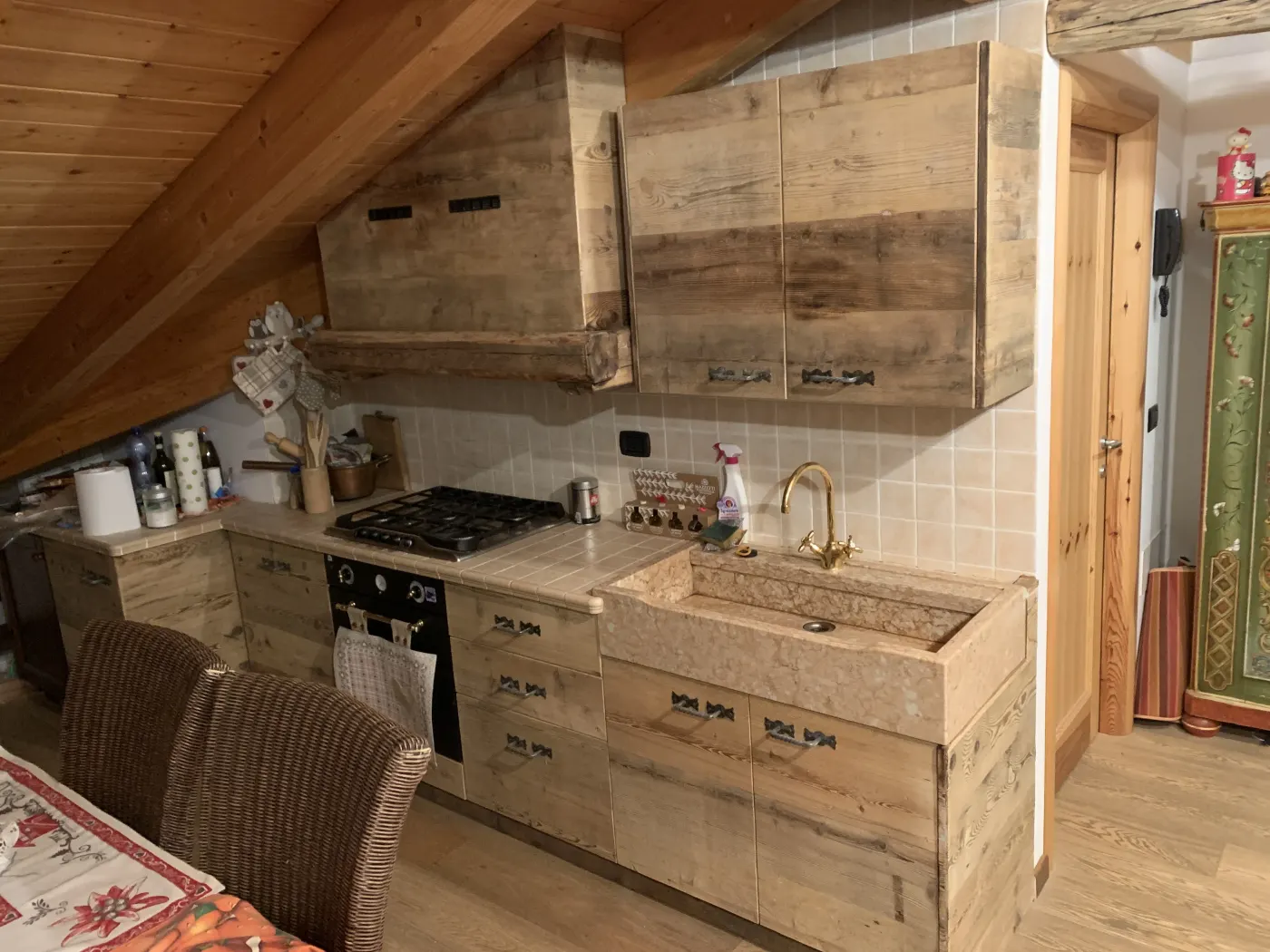 Cucina in mansarda con travi a vista, cappa e ante in legno antico e lavello in pietra naturale