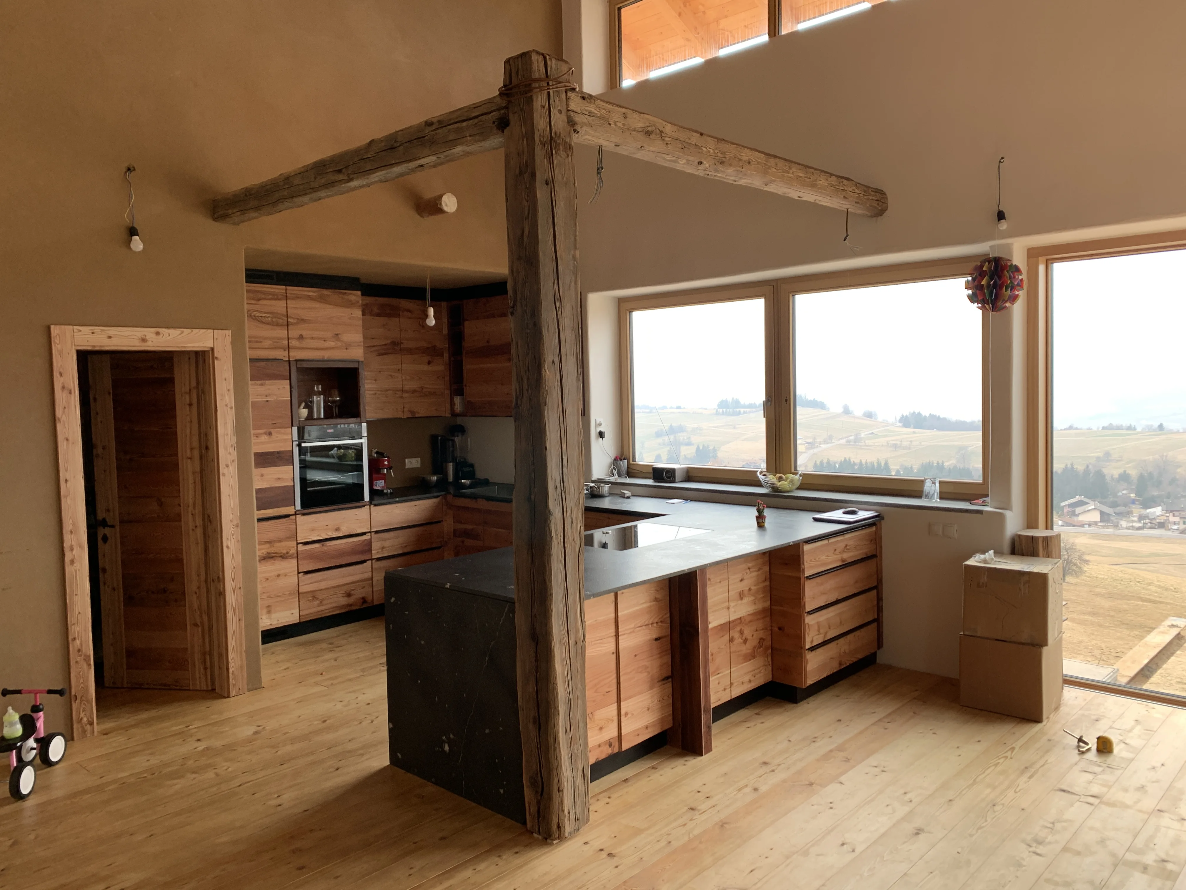 Cucina a isola in legno antico con trave a vista e ampie vetrate affacciate sulle montagne