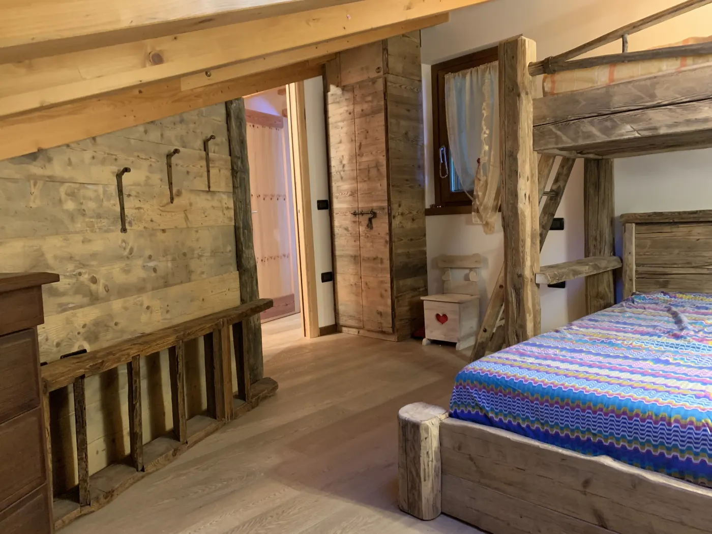 Camera con letto a soppalco in legno antico, appendiabiti a muro e porta scorrevole