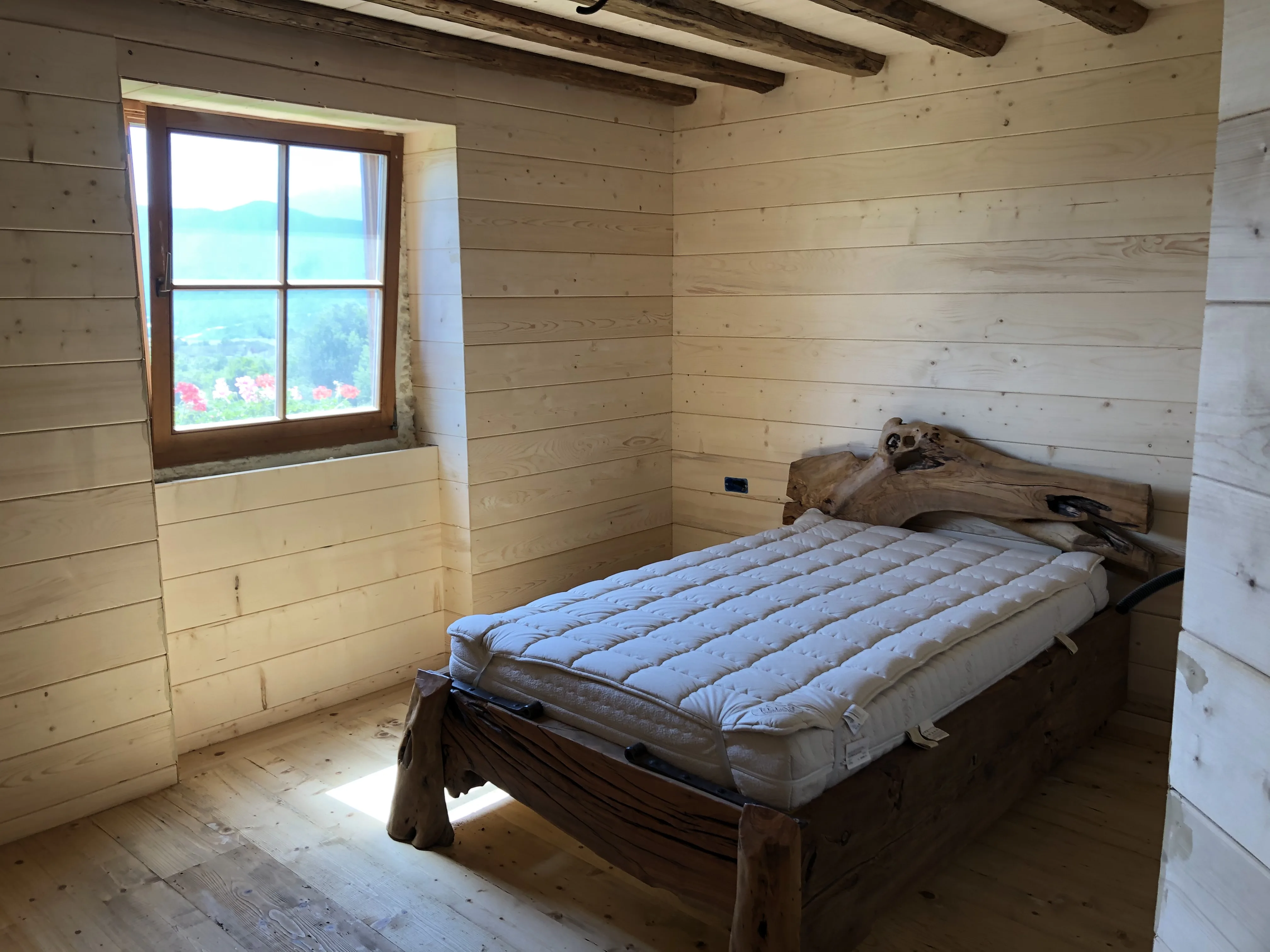 Camera in boiserie di legno chiaro con testata del letto in radica e vista sulle colline