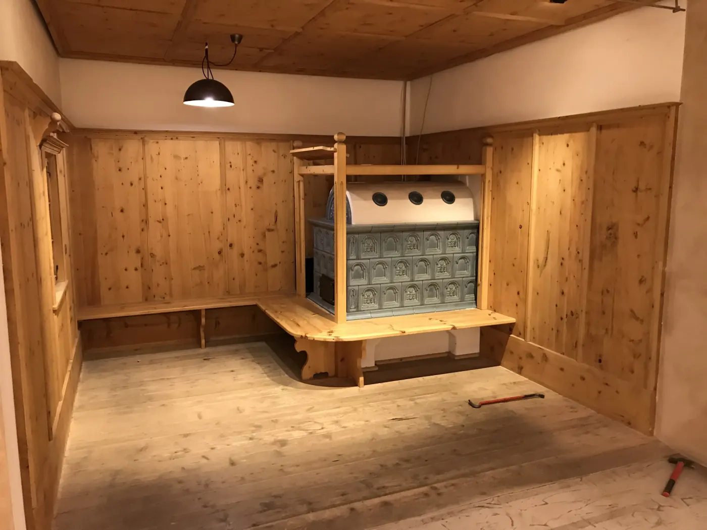 Stube tradizionale in legno chiaro con panche perimetrali e stufa in maiolica